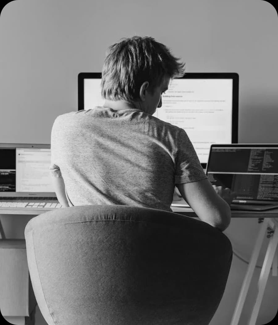 View from behind of a person sitting at a desk with multiple monitors and laptops.