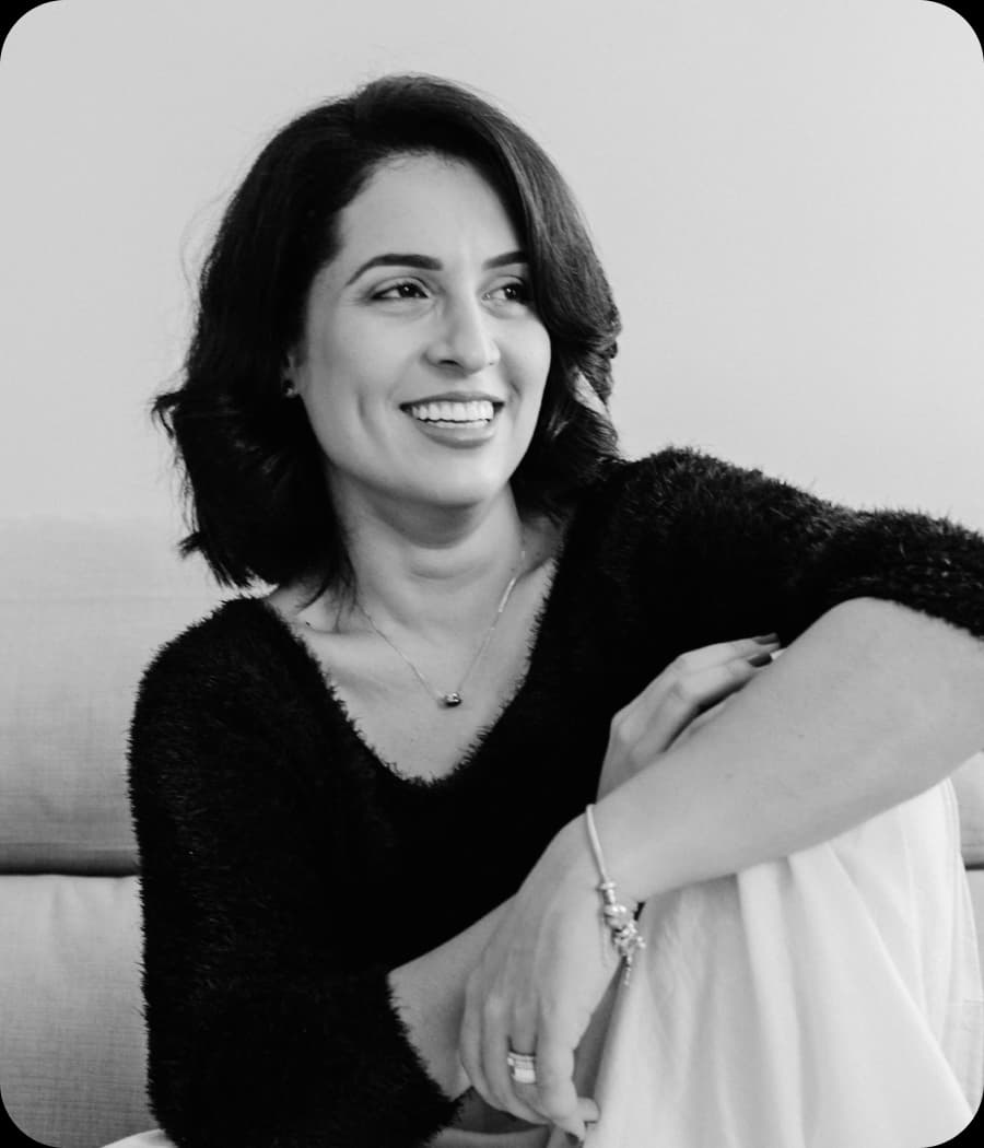 Woman in a dark top smiling and looking away, one leg crossed.